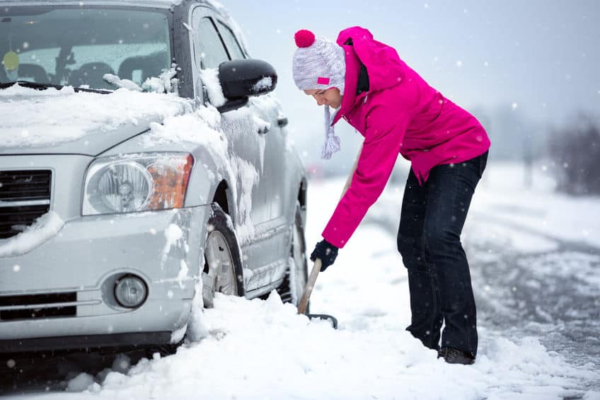 Woman shovels her car out of the snow. Winter driving preparedness.